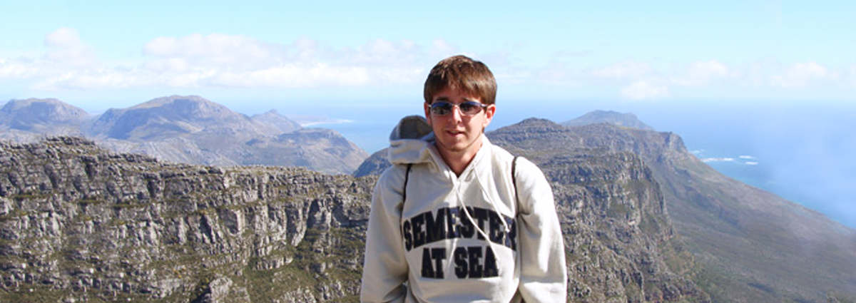 A Cabrini student wearing a Semester at Sea sweatshirt on a mountain top